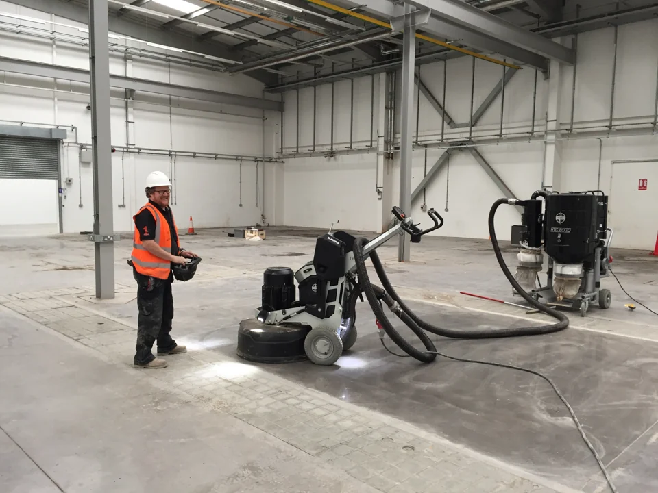 Professional floor grinder connected to a dust extractor in an industrial unit.